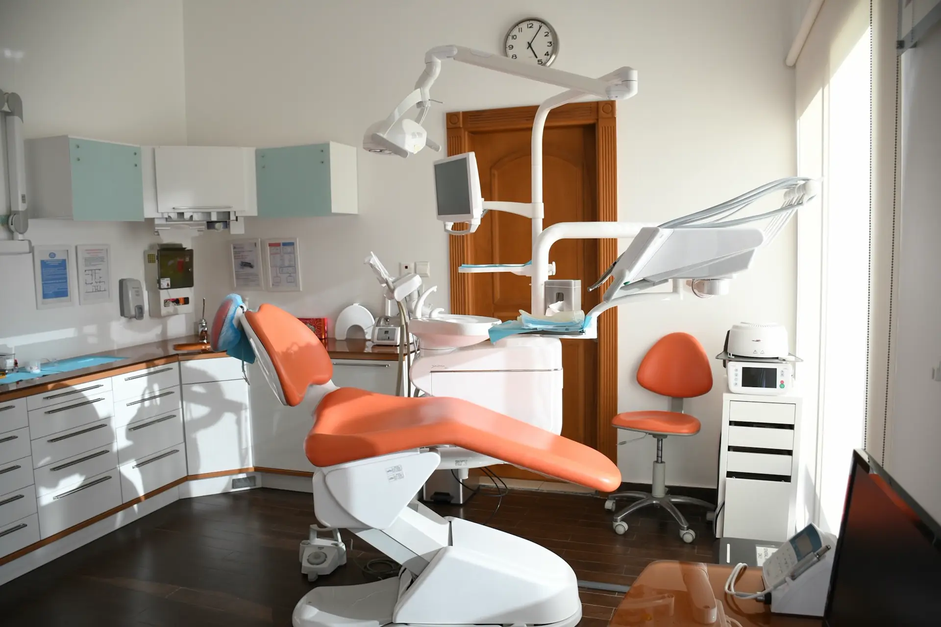 Gabinete de la clínica: sillón tapizado en naranja, lámpara y una ventana grande con luz de mañana.